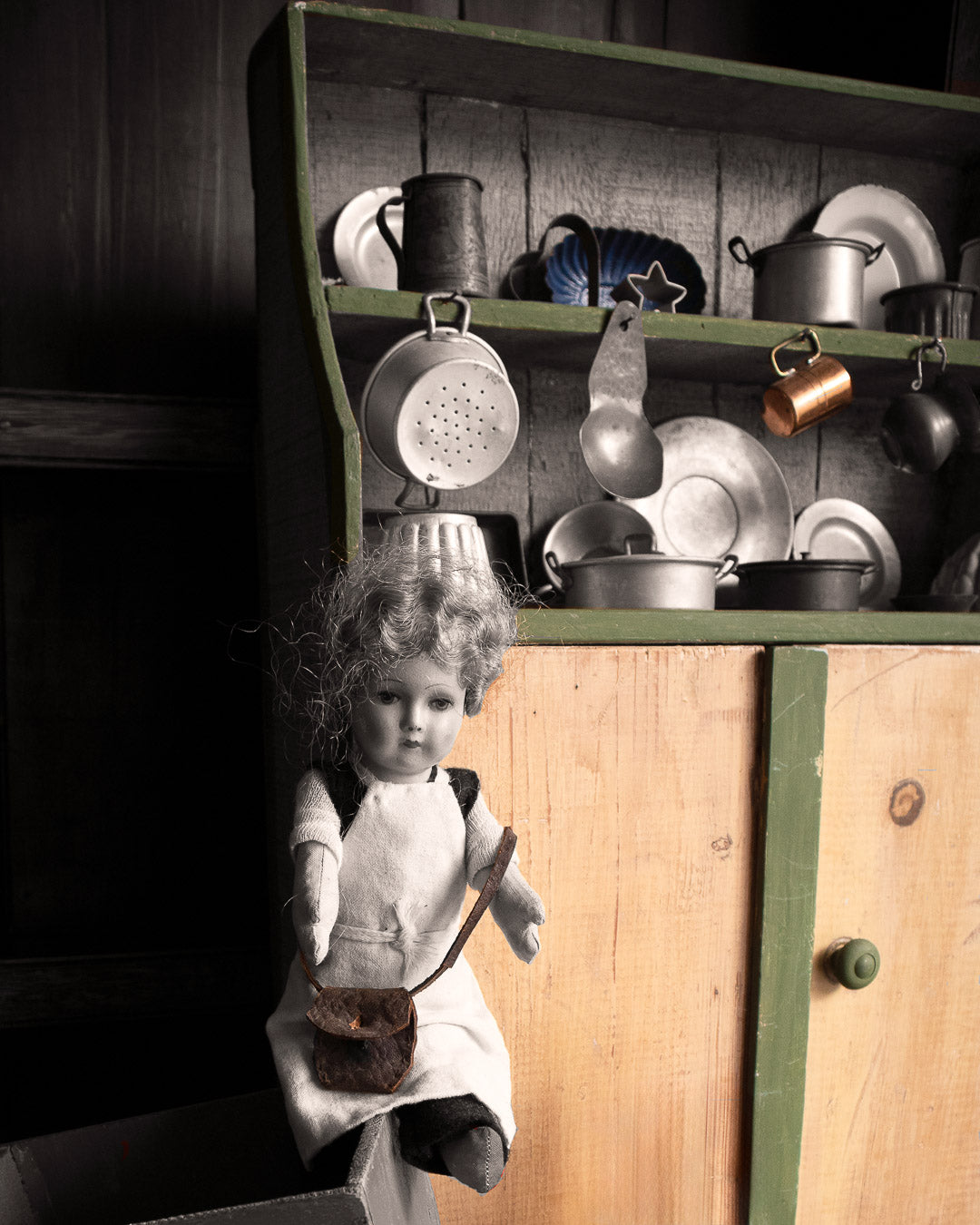 Doll with a kitchen dresser containing kitchen items on a black and white background