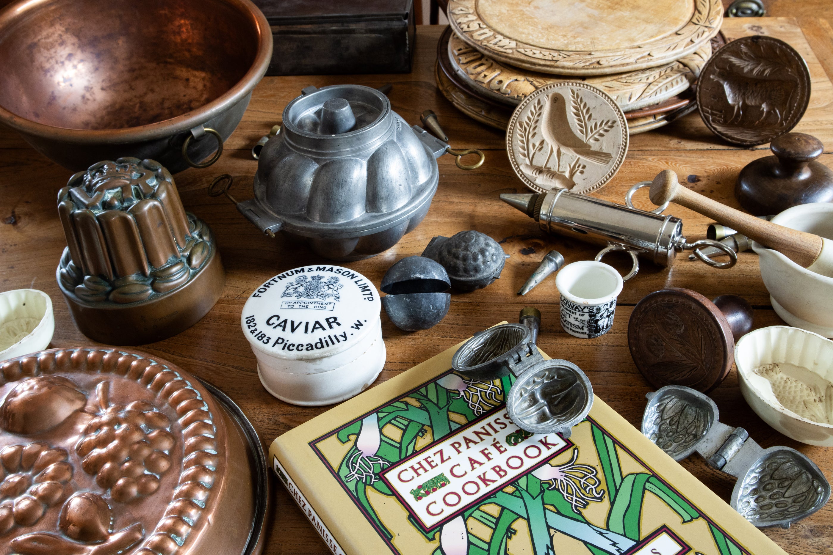 Table with a collection of kitchen items including copper bowl, breadboards, cookbook, butter prints and cooking moulds