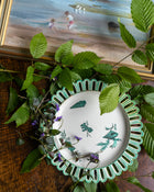 Decorative Wedgwood plate with floral design on a table with leaves and a painting in the background