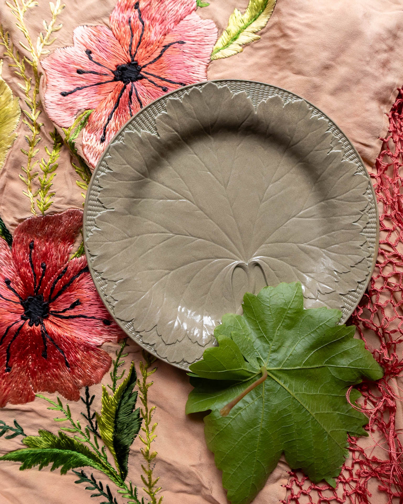 Decorative Wedgwood drabware plate with leaf design on a floral fabric background