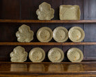 Set of Wedgwood ceramic leaf-patterned plates on wooden shelves.