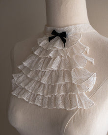 White lace jabot with a black bow on a mannequin against a neutral background