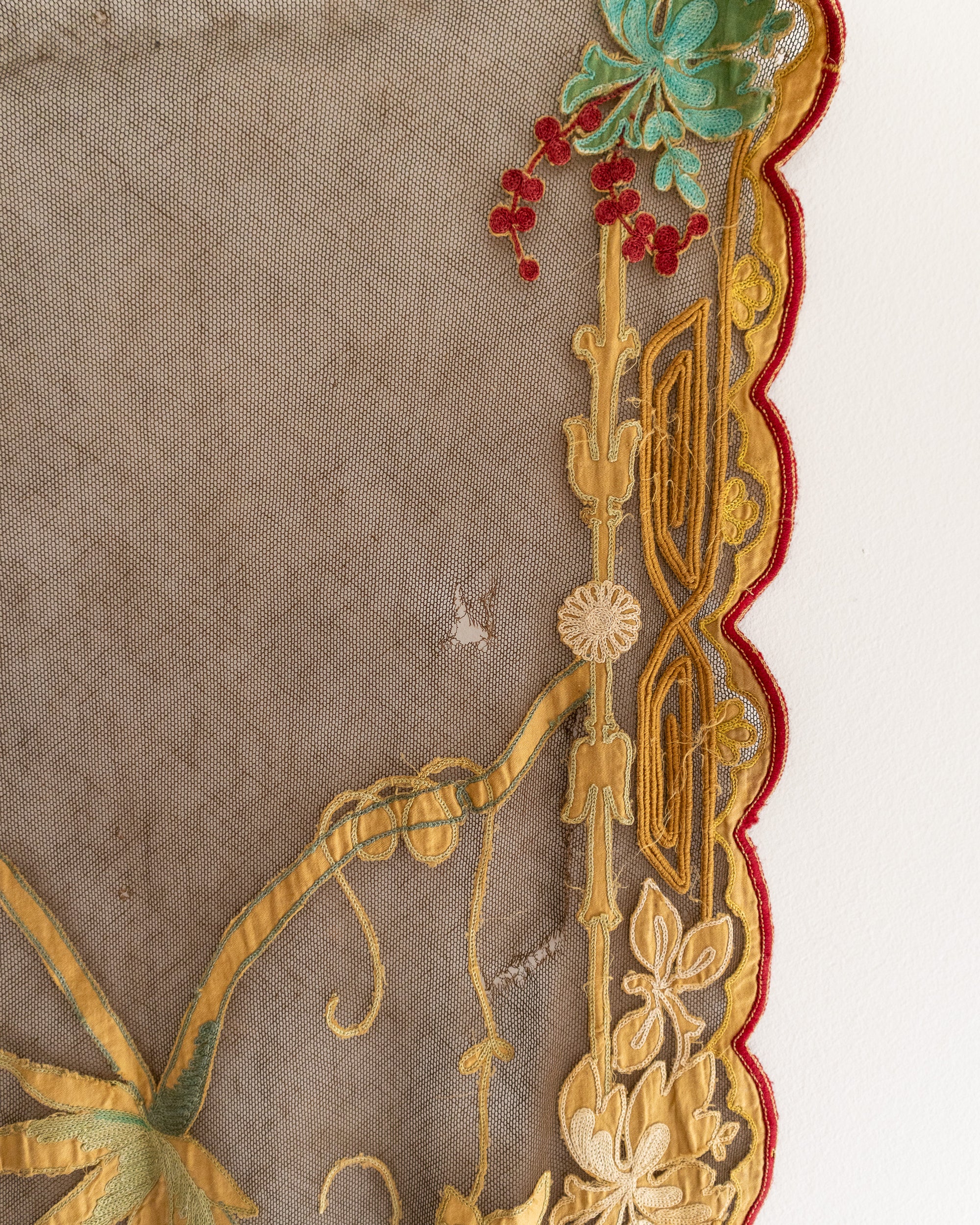 Close-up of intricate embroidery with gold, red, and green details on a brown fabric background.