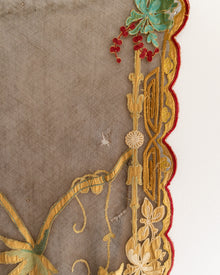 Close-up of intricate embroidery with gold, red, and green details on a brown fabric background.