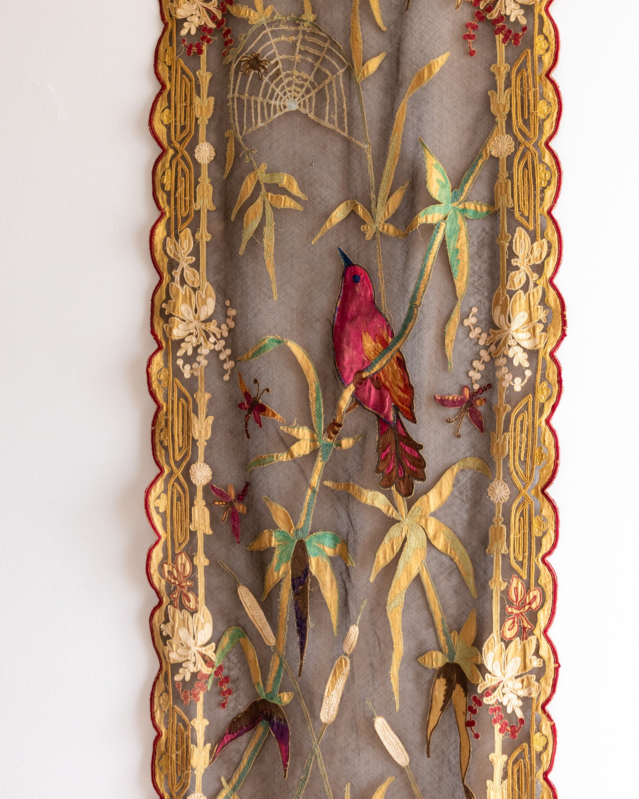 Decorative panel with embroidered bird, flowers, and spider web on a plain background