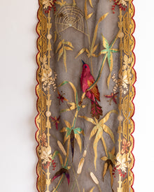 Decorative panel with embroidered bird, flowers, and spider web on a plain background