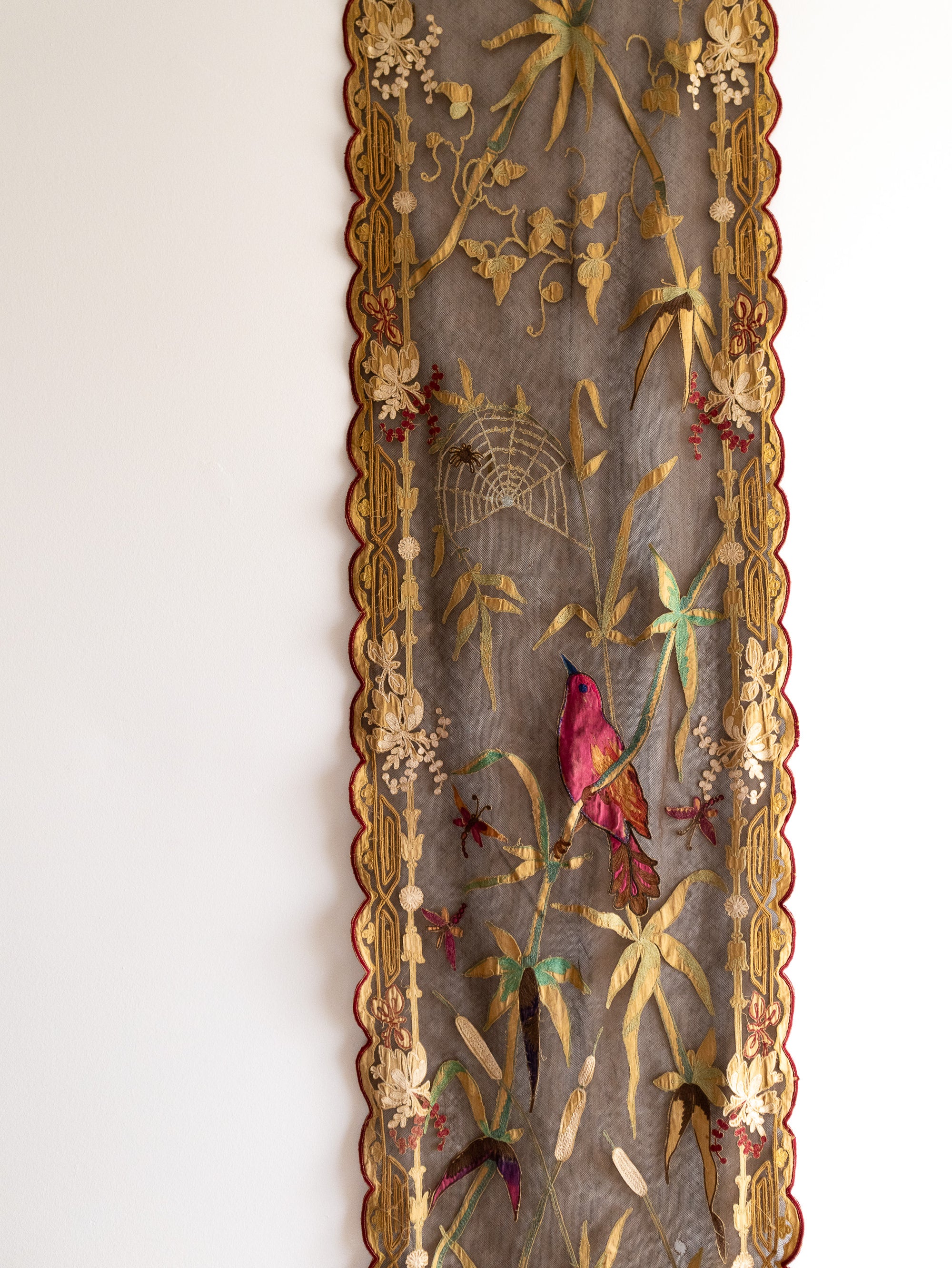 Decorative fabric panel with embroidered birds and flowers in a gold frame on a white background
