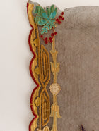 Decorative lace trim with gold, red, and green patterns on a textured fabric background.