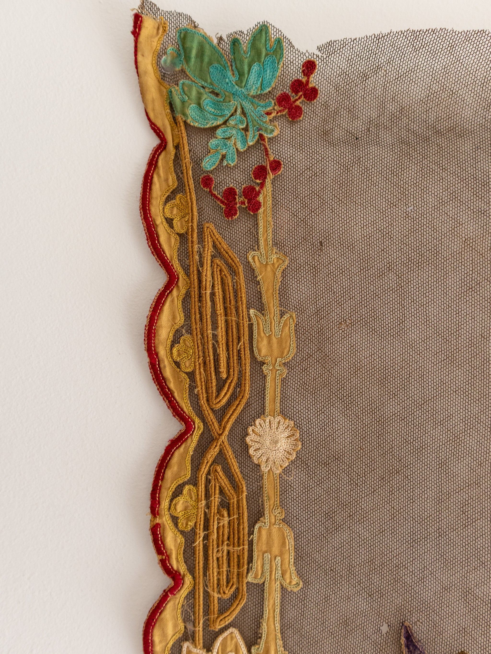 Decorative lace trim with gold, red, and green patterns on a textured fabric background.