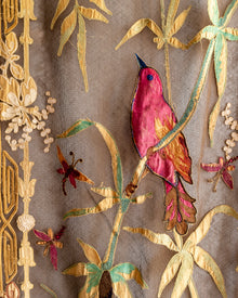 Embroidered fabric with a red bird and gold leaves on a brown background