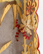 Close-up of embroidered fabric with gold and red floral patterns on a beige background