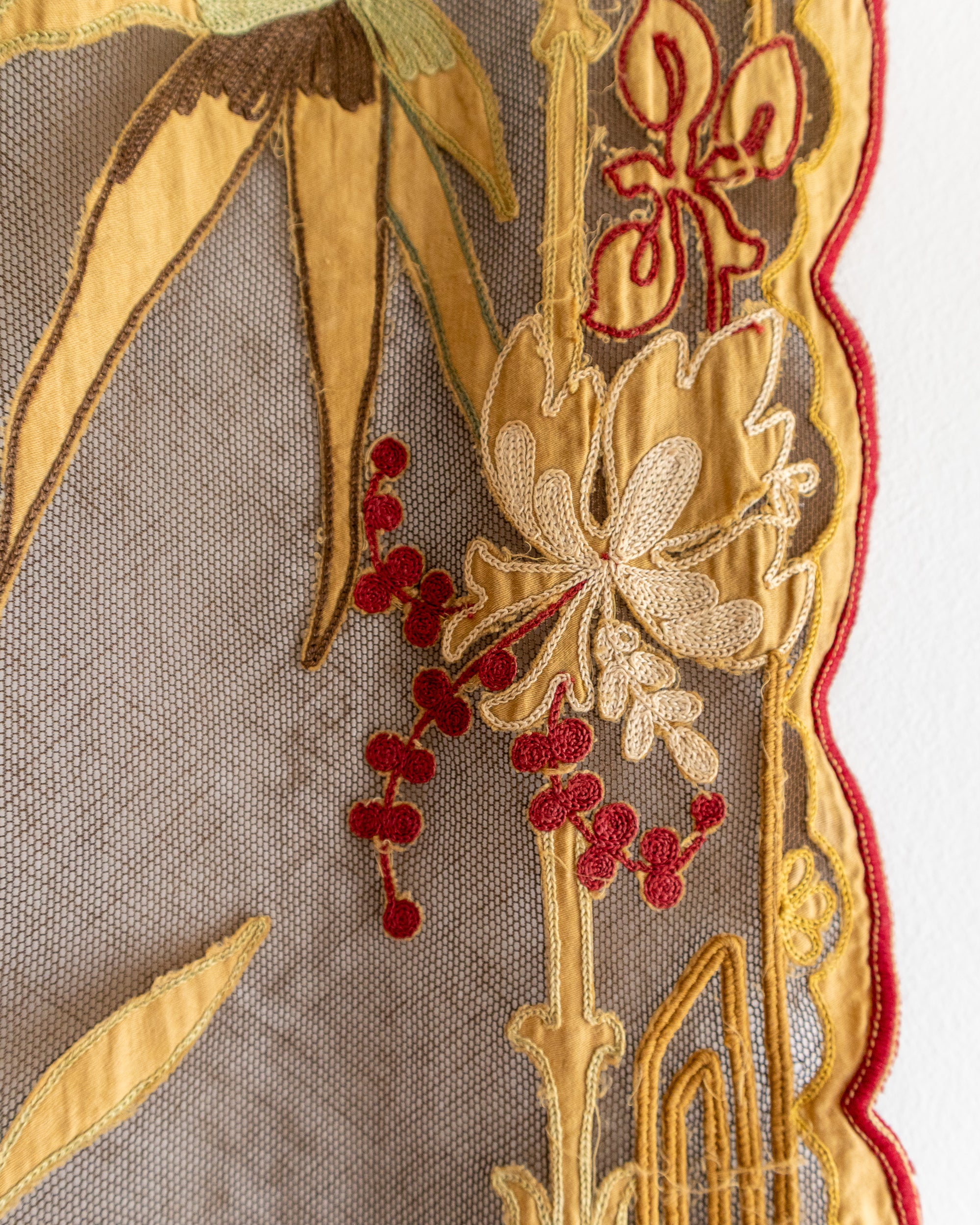 Close-up of embroidered fabric with gold and red floral patterns on a beige background