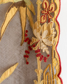 Close-up of embroidered fabric with gold and red floral patterns on a beige background