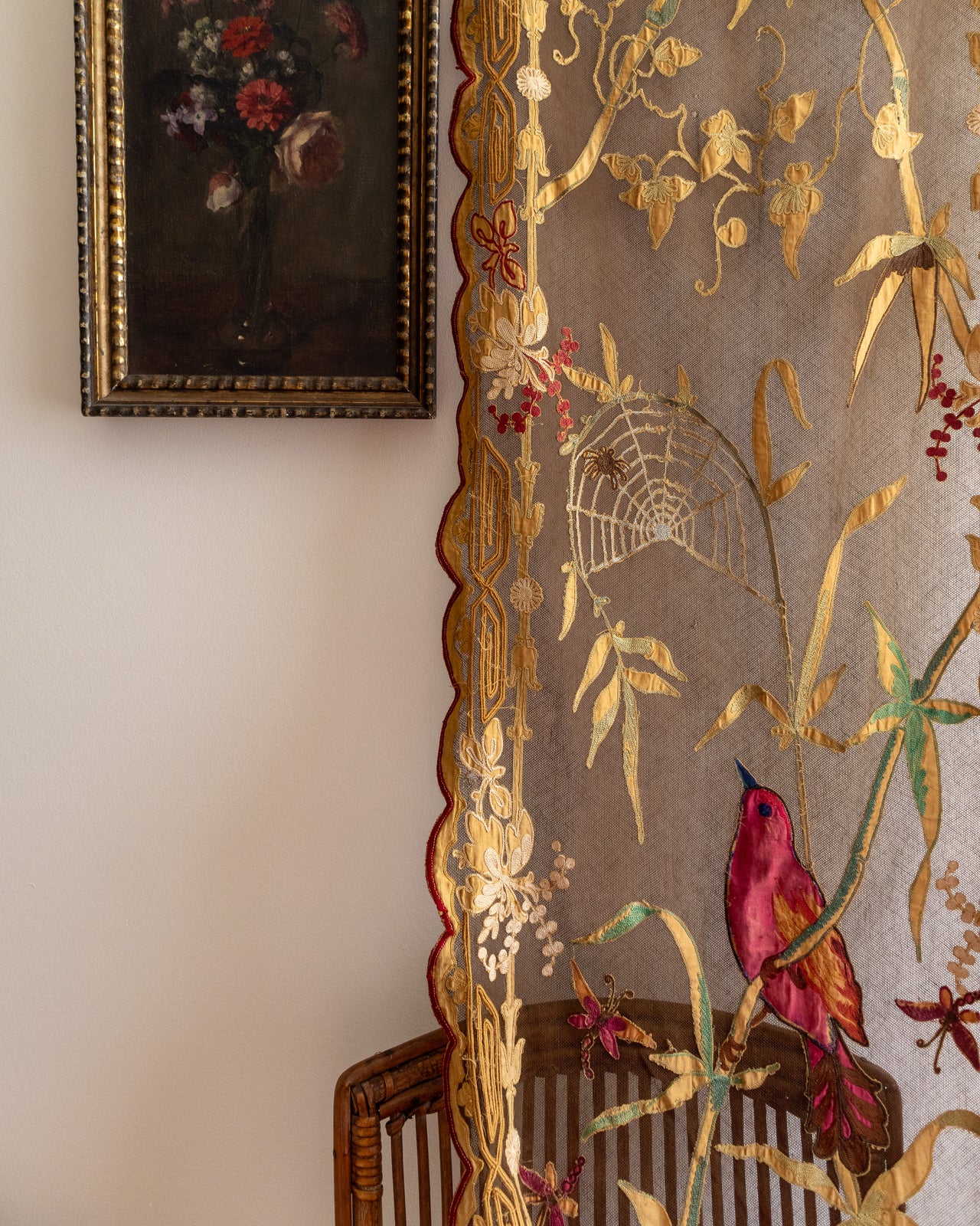 Decorative fabric with floral and bird patterns on a chair, with a painting in the background.