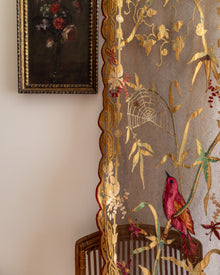 Decorative fabric with floral and bird patterns on a chair, with a painting in the background.