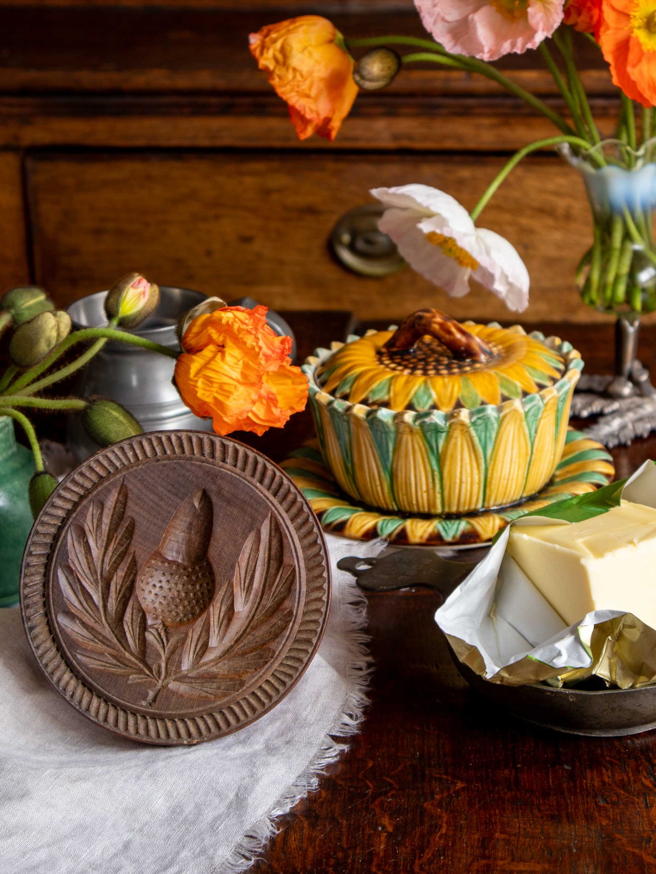 Decorative items including a wooden butter stamp, ceramic bowl with floral design, and flowers on a wooden surface.