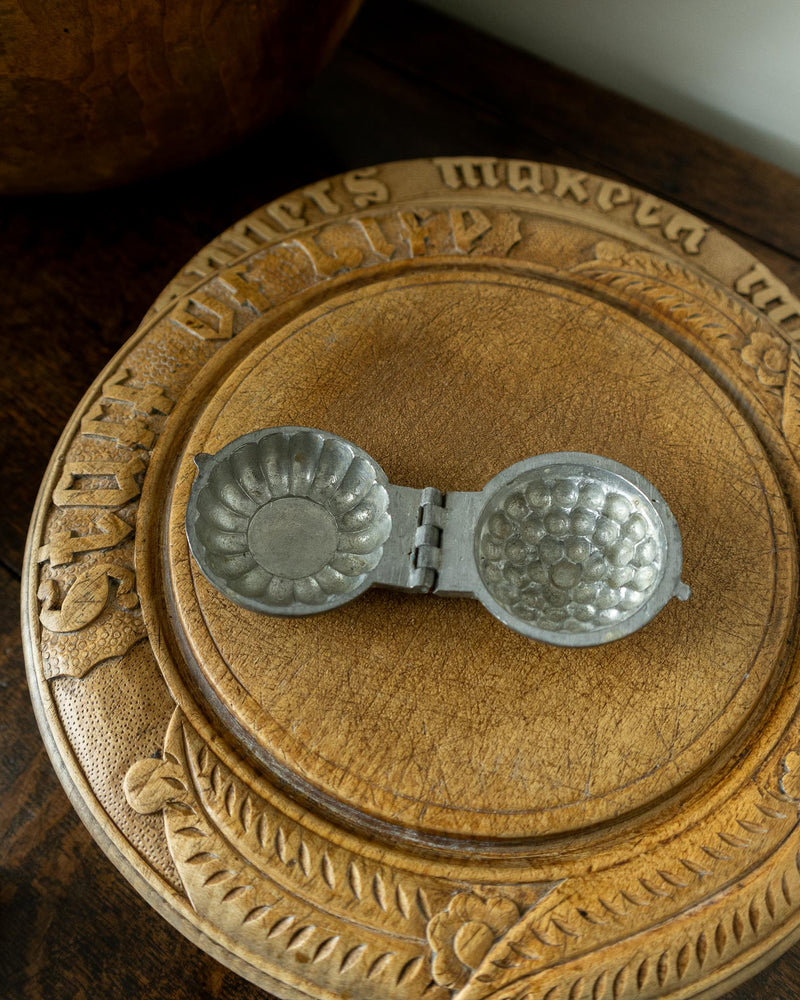 Decorative wooden breadboard with a pewter mould on a dark background