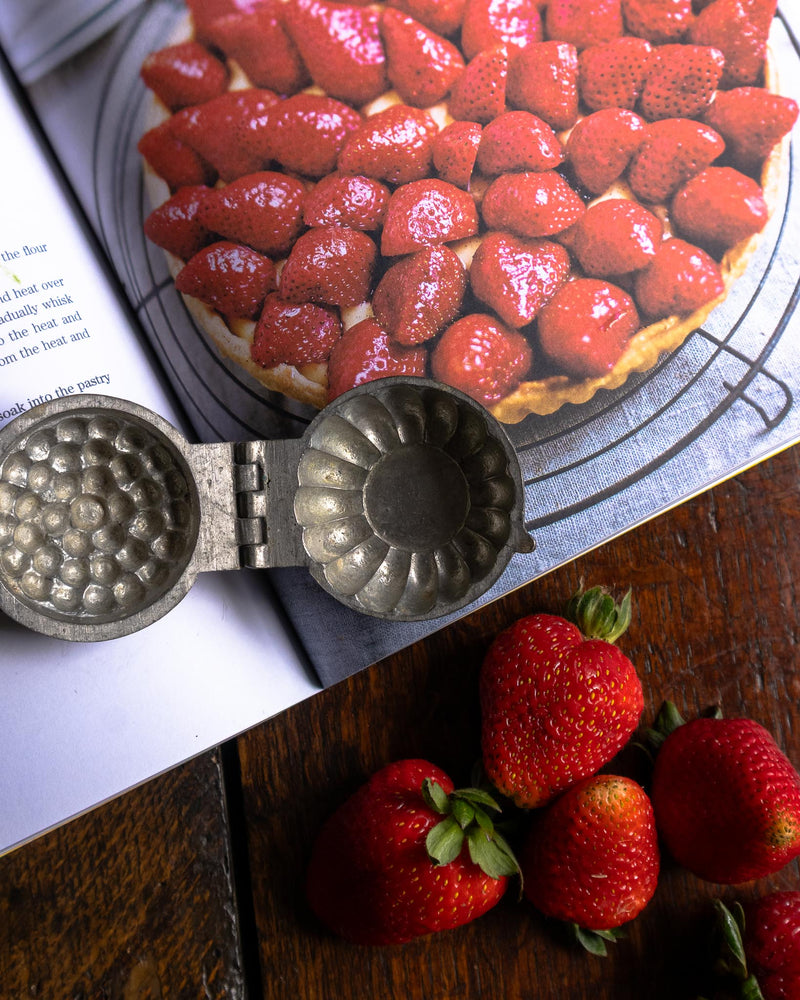 Strawberry tart with a pewter mould on a wooden surface