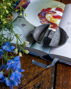 Decorative items including a pewter mould, blue flowers, and an open book on a wooden surface.