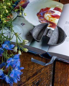 Decorative items including a pewter mould, blue flowers, and an open book on a wooden surface.