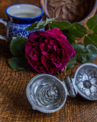 Rose-shaped pewter mould, pink rose, and blue teacup on a wooden surface