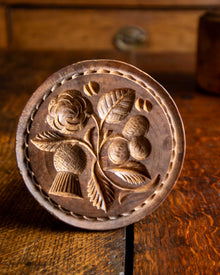 Wooden butter stamp with floral design on a wooden surface