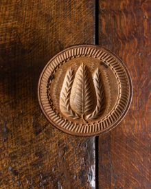 Wooden butter stamp with leaf design on a wooden surface