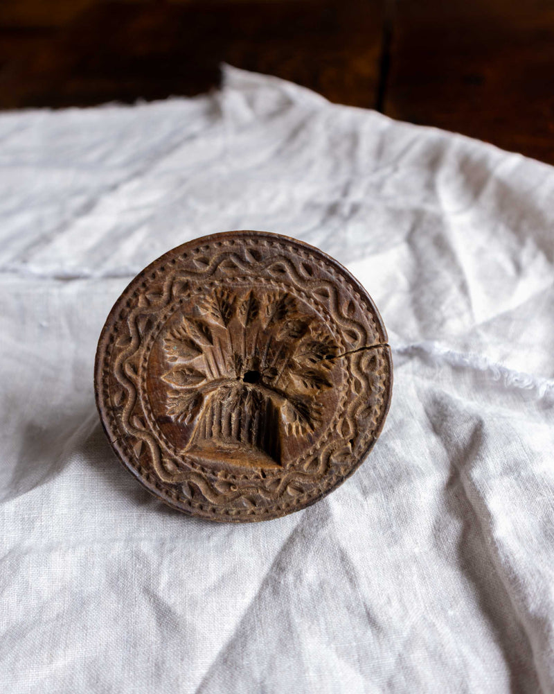 Wooden butter stamp with intricate design on a white fabric background