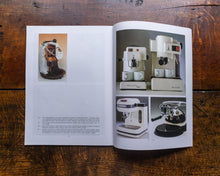 Open book on a wooden surface with images of vintage coffee machines.
