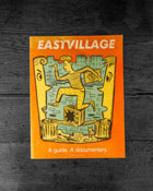 Book cover of 'Eastvillage' with illustration of a person climbing a wall on an orange background