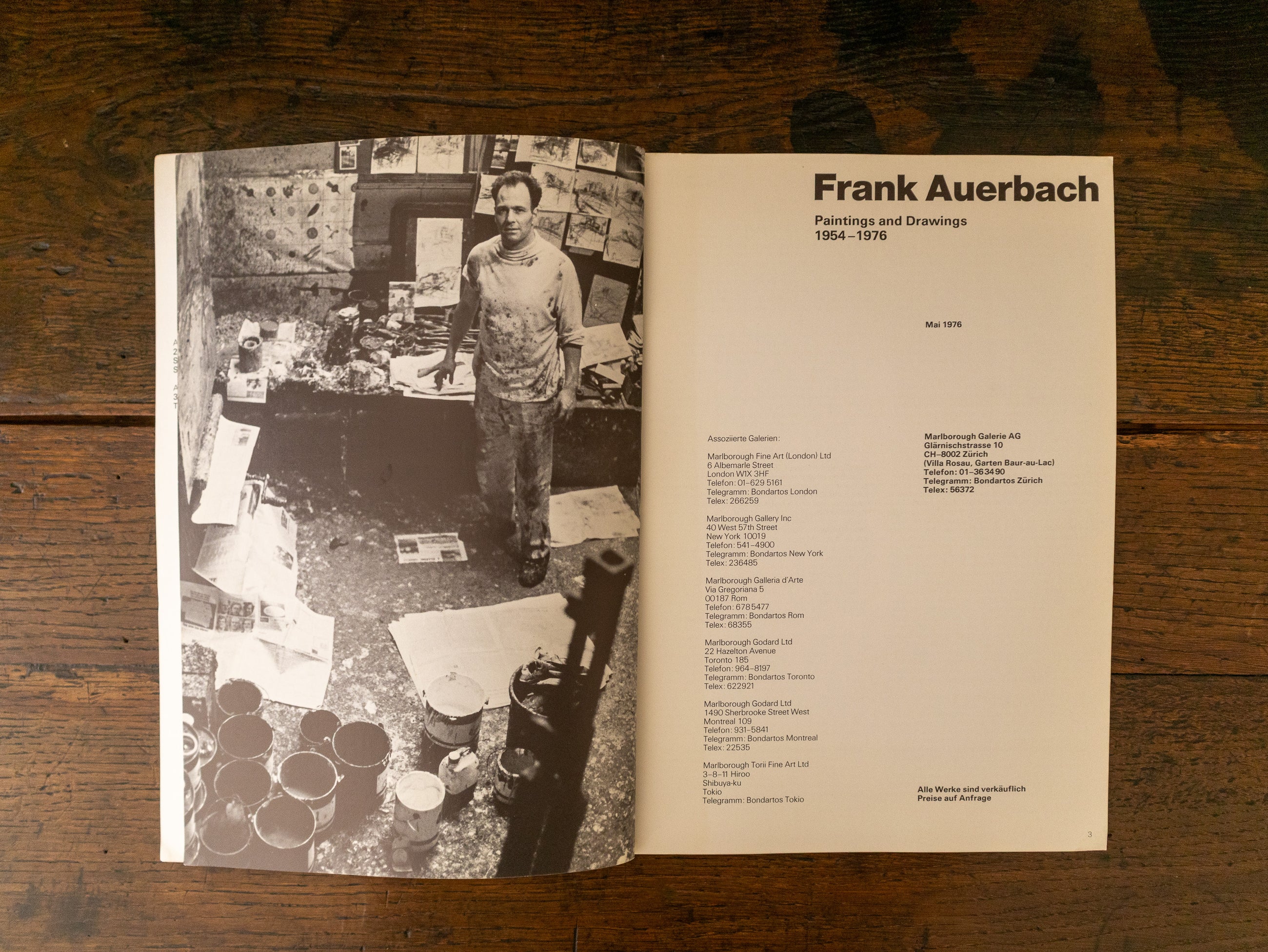 Open book showing a black and white photo of Frank Auerbach in a studio and text on a wooden surface
