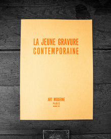 Book cover with text 'LA JEUNE GRAVURE CONTEMPORAINE' on a dark wooden surface