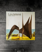 Book cover of 'Louisiana' with a sculpture and landscape on a wooden surface