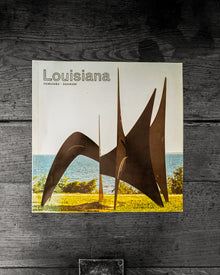 Book cover of 'Louisiana' with a sculpture and landscape on a wooden surface