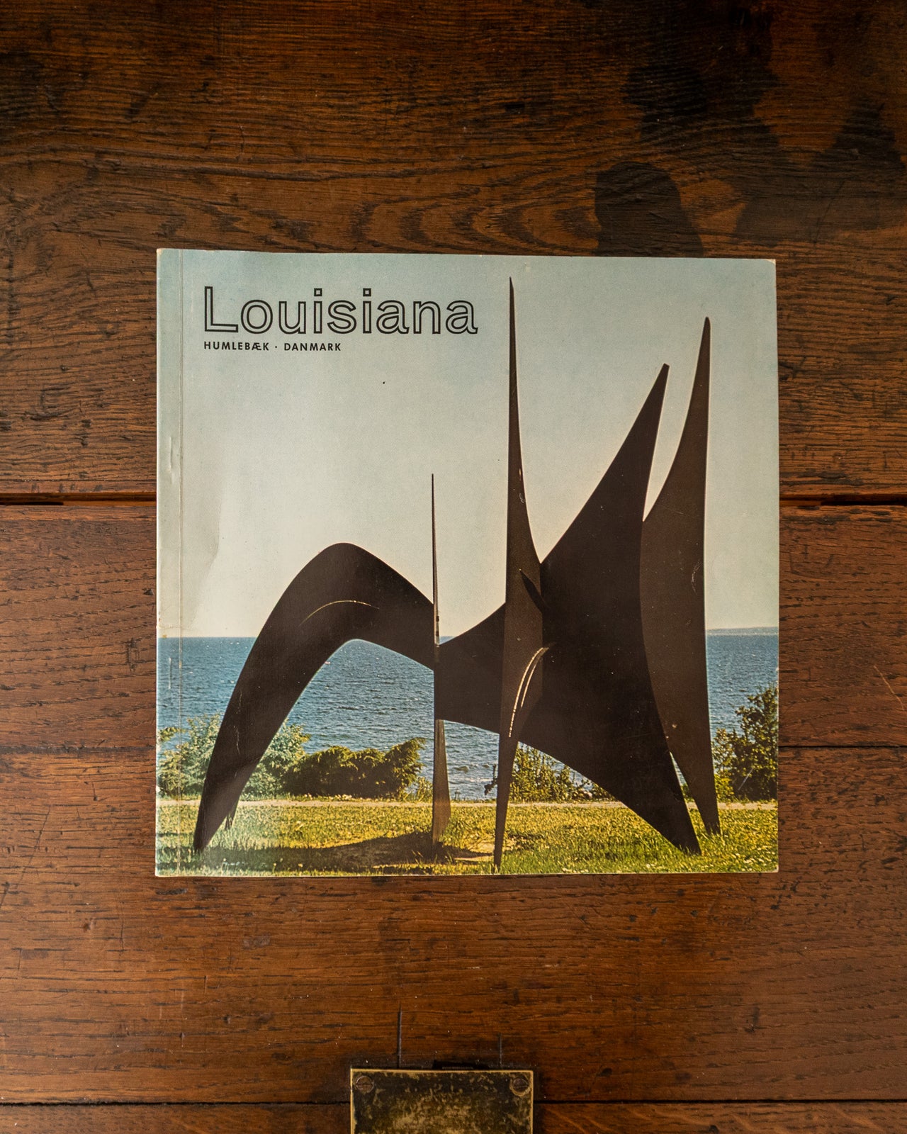 Book titled 'Louisiana' with a sculpture on the cover, placed on a wooden surface.