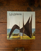 Book titled 'Louisiana' with a sculpture on the cover, placed on a wooden surface.