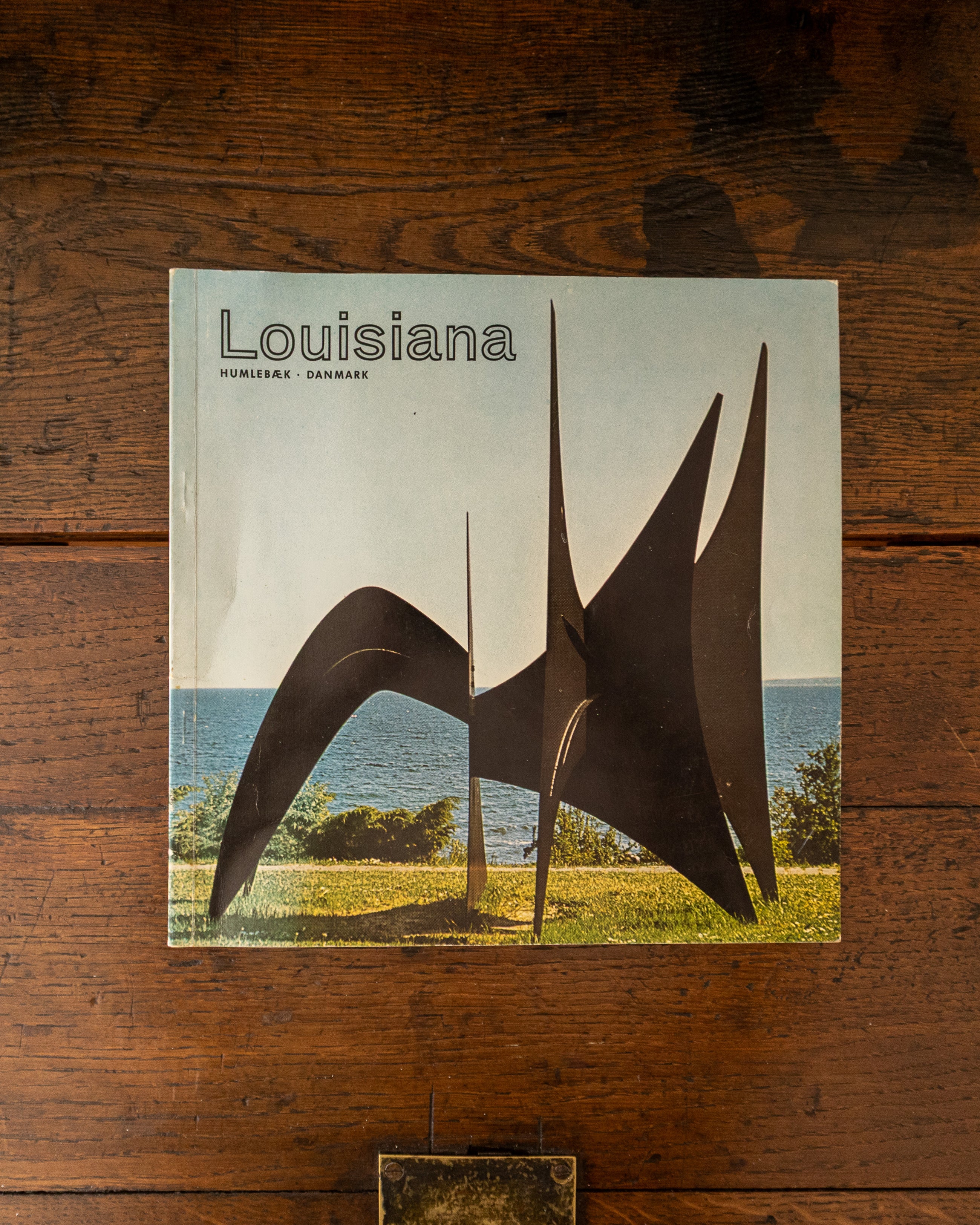 Book titled 'Louisiana' with a sculpture on the cover, placed on a wooden surface.