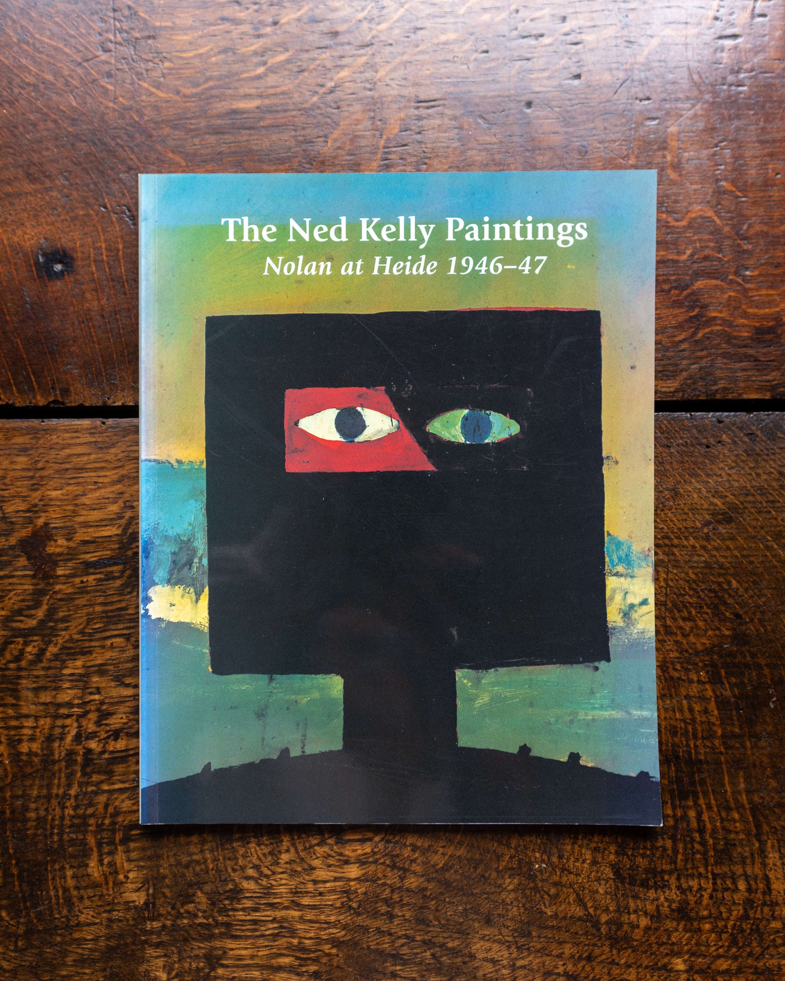 Book cover of 'The Ned Kelly Paintings' by Nolan at Heide 1946-47 on a wooden surface