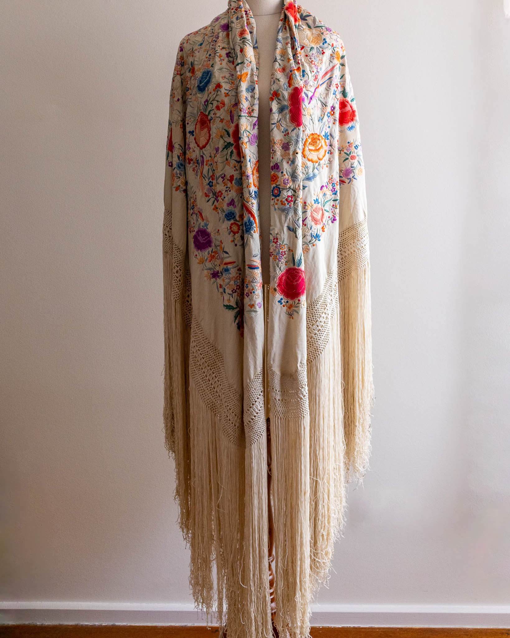 Floral patterned scarf with fringe on a mannequin against a plain background