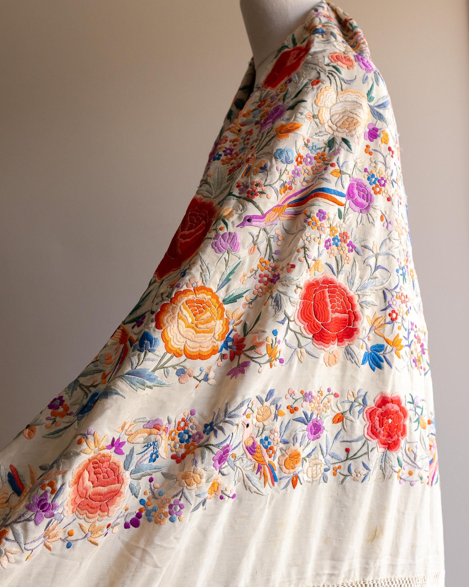 Colorful floral embroidery on a white fabric draped over a mannequin against a neutral background