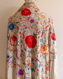 Colorful floral and embroidered scarf on a mannequin against a plain background