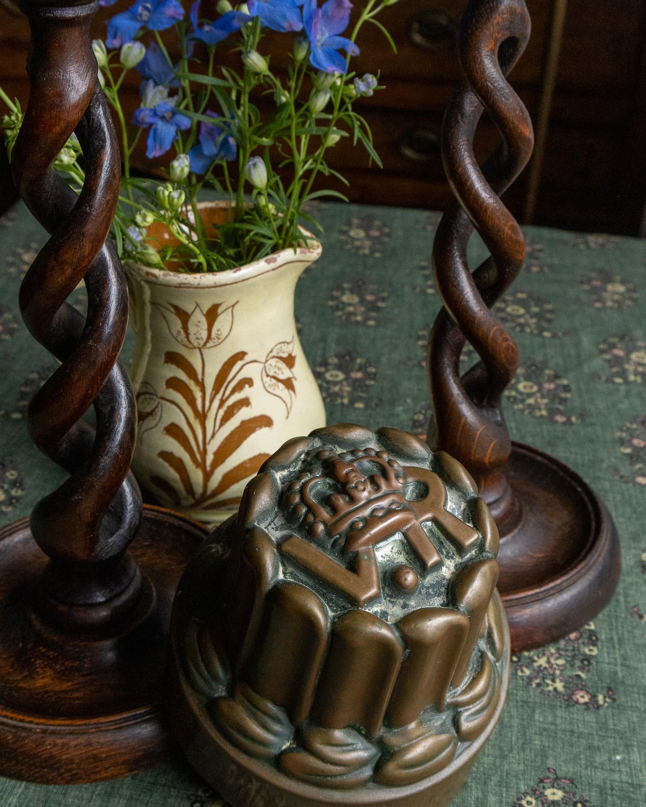 Decorative vase with flowers, wooden candlesticks, and decorative copper mould on a patterned surface