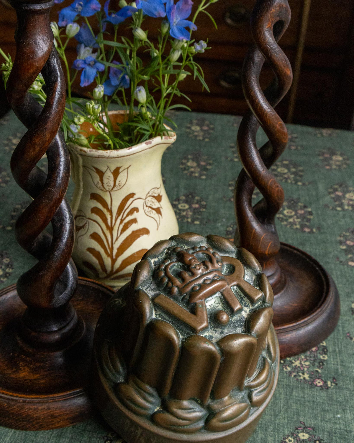 Decorative vase with flowers, wooden candlesticks, and decorative copper mould on a patterned surface